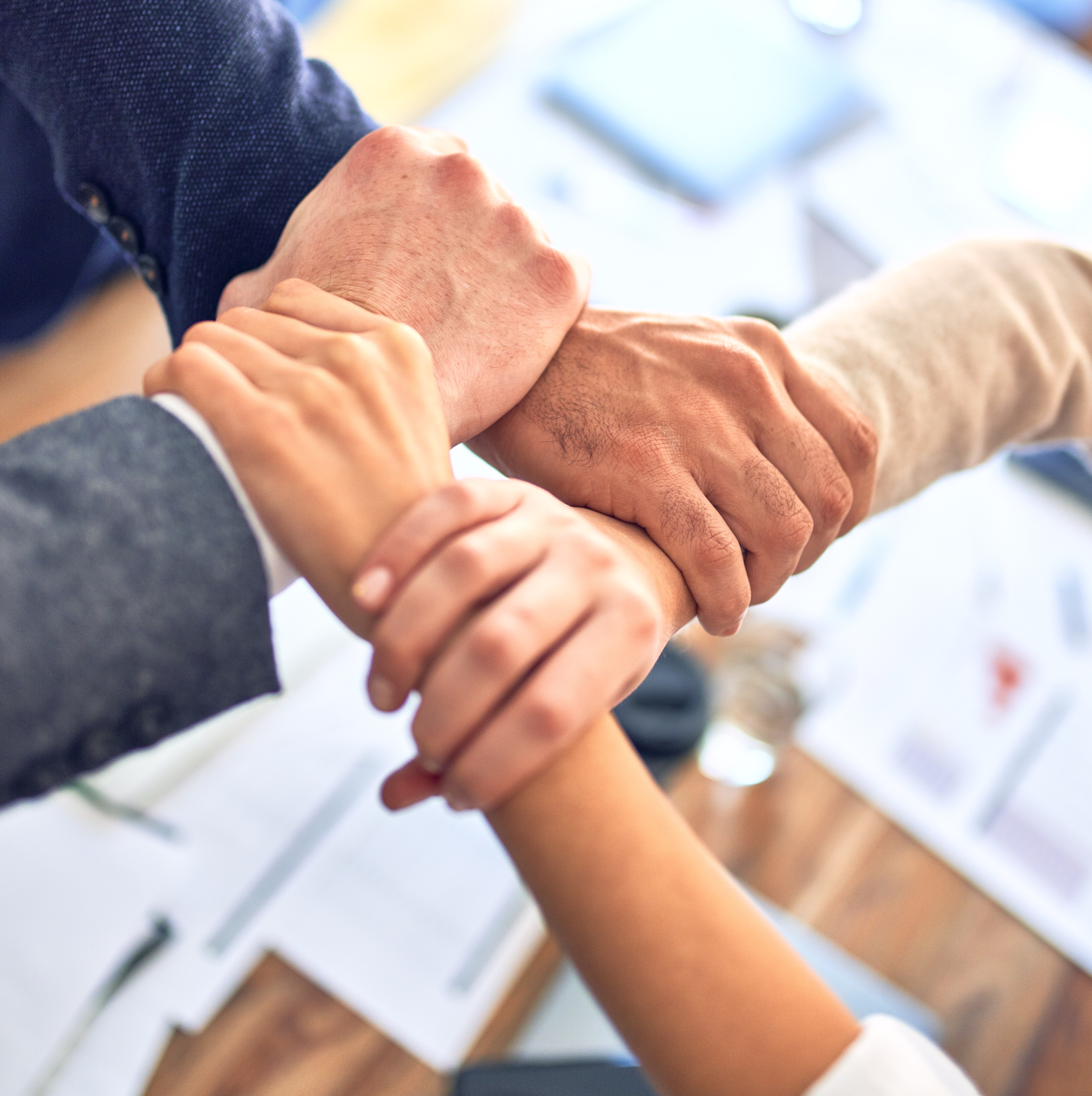 Interlocking hands over business documents symbolizing teamwork (Photo by Krakenimages, Unsplash)